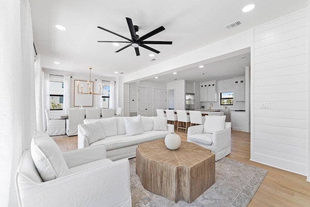living room featuring light wood finished floors, ceiling fan with notable chandelier, visible vents, and recessed lighting