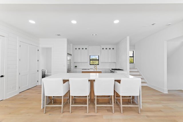 kitchen with built in refrigerator, white cabinetry, a breakfast bar area, and light wood-style floors