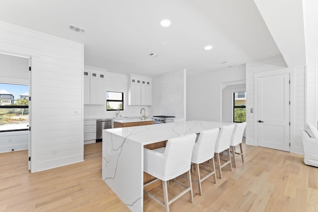 kitchen featuring visible vents, light wood-style flooring, light stone countertops, appliances with stainless steel finishes, and glass insert cabinets