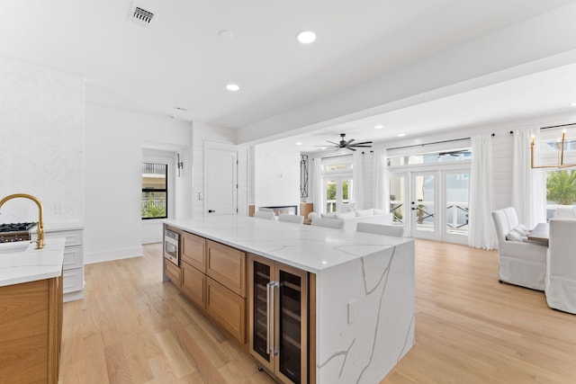 kitchen with open floor plan, stainless steel microwave, light wood-style floors, beverage cooler, and visible vents