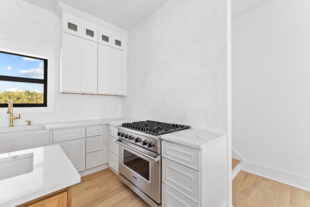 kitchen with tasteful backsplash, high end stainless steel range oven, light wood-style flooring, light stone countertops, and glass insert cabinets