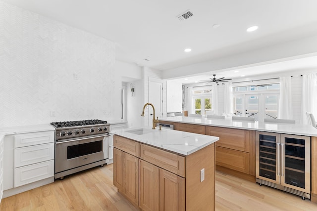 kitchen featuring high end stainless steel range, a sink, a center island with sink, beverage cooler, and visible vents