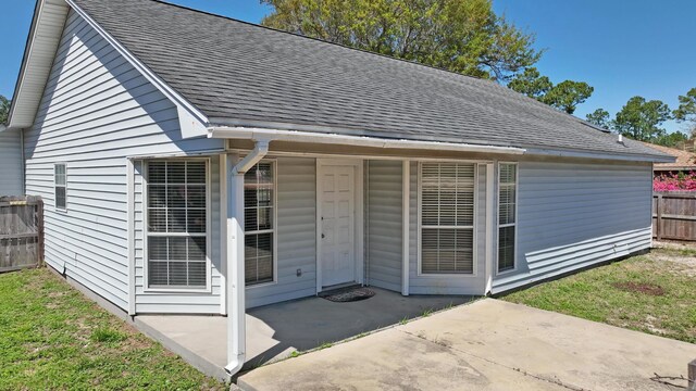 view of exterior entry with fence, a patio, and roof with shingles