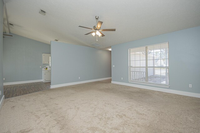 carpeted empty room with vaulted ceiling, a textured ceiling, baseboards, visible vents, and ceiling fan