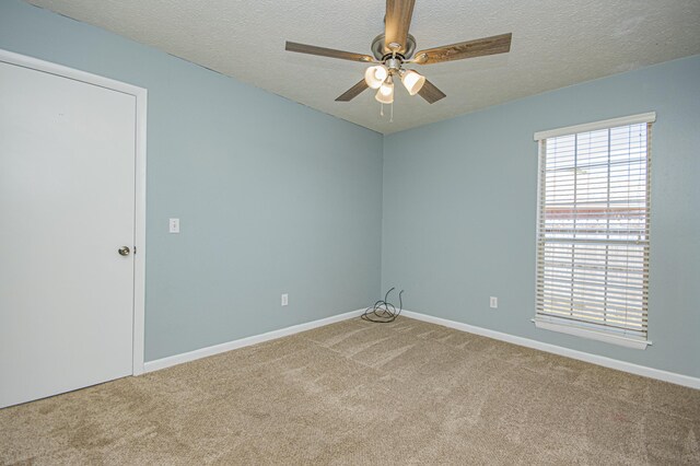 carpeted empty room with a textured ceiling, ceiling fan, and baseboards