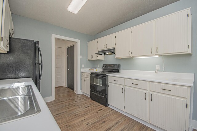 kitchen with light countertops, a textured ceiling, light wood-type flooring, under cabinet range hood, and black appliances