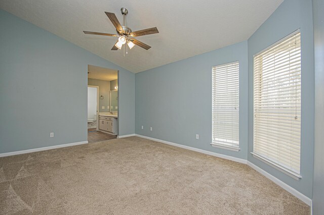 unfurnished bedroom with carpet flooring, a textured ceiling, lofted ceiling, ensuite bath, and baseboards