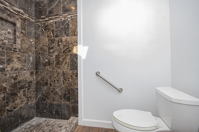 full bath with toilet, baseboards, tiled shower, and wood finished floors