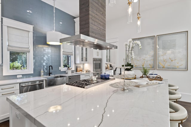kitchen featuring wall chimney exhaust hood, a sink, a towering ceiling, a kitchen bar, and appliances with stainless steel finishes