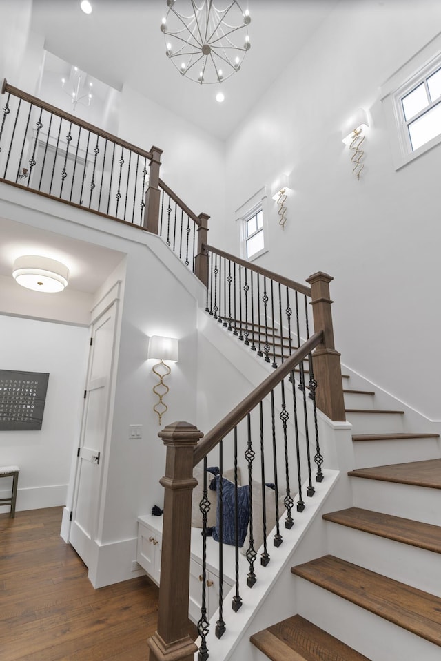 stairs with recessed lighting, a high ceiling, wood finished floors, baseboards, and a notable chandelier