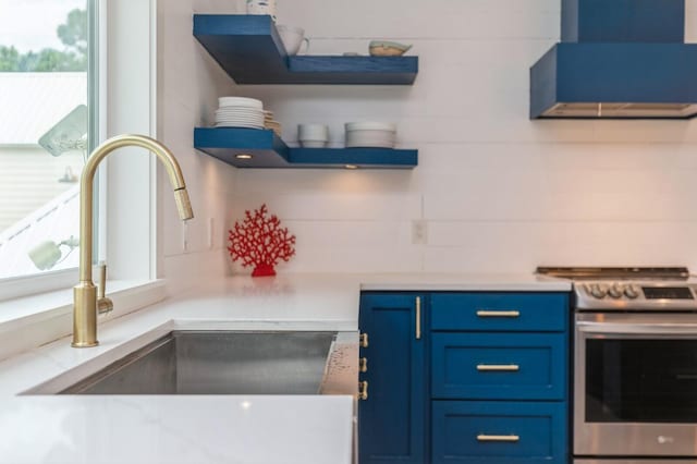 kitchen featuring a sink, open shelves, wall chimney exhaust hood, stainless steel electric stove, and blue cabinetry