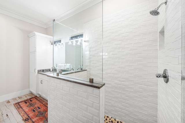 full bath featuring tiled shower, vanity, baseboards, and ornamental molding