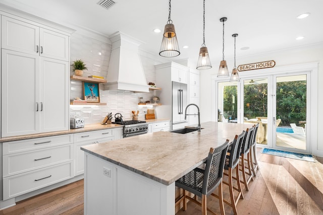 kitchen featuring light wood-style flooring, premium range hood, visible vents, premium appliances, and a sink