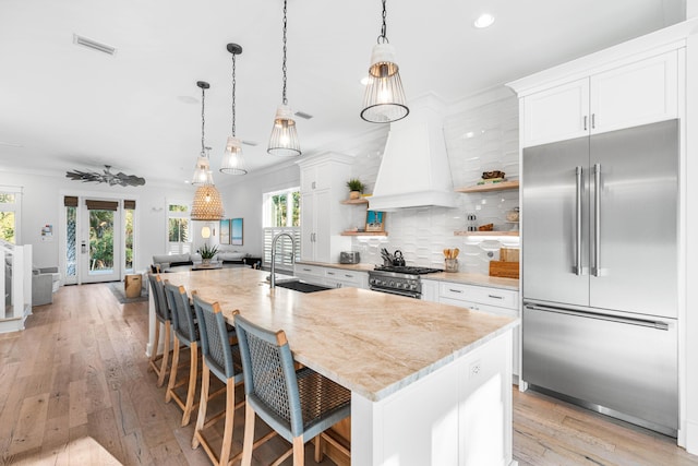 kitchen with open shelves, visible vents, custom exhaust hood, a sink, and high quality appliances