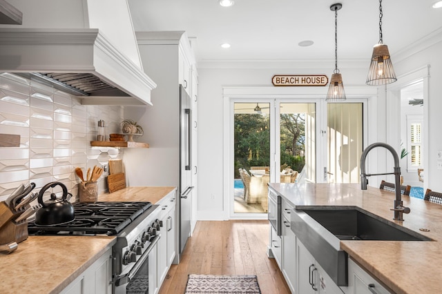 kitchen featuring pendant lighting, high end stainless steel range, custom exhaust hood, a sink, and light wood finished floors