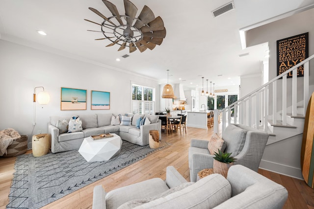 living room with visible vents, ornamental molding, a ceiling fan, light wood finished floors, and stairs