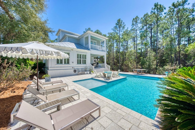 rear view of house with a balcony, an outdoor pool, a patio area, a standing seam roof, and metal roof