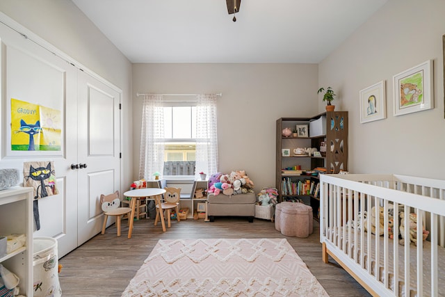 bedroom with a crib, ceiling fan, a closet, and wood finished floors