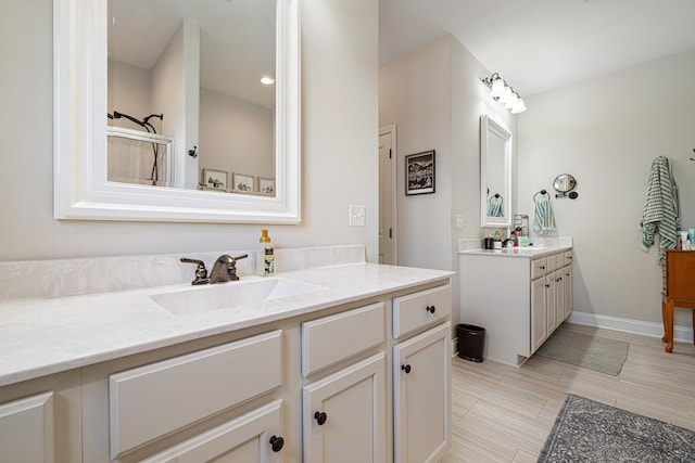 full bathroom with a sink, baseboards, an enclosed shower, and two vanities