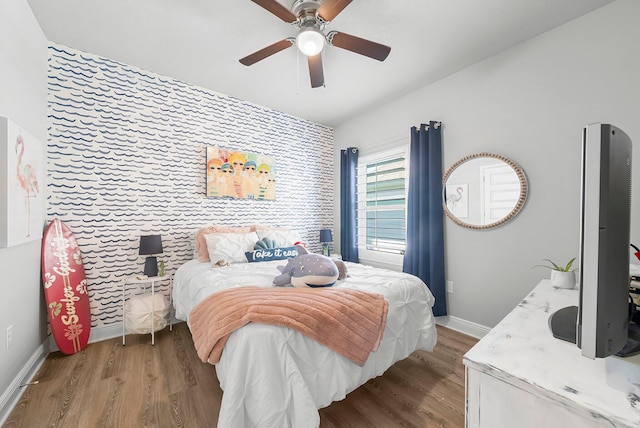 bedroom with baseboards, ceiling fan, an accent wall, and wood finished floors