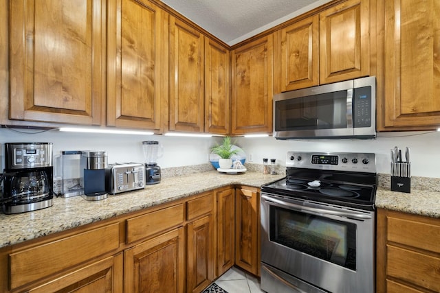 10 Mar A Lago Blvd # 14, Santa Rosa Beach, FL 32459 - kitchen with brown cabinetry, a textured ceiling, appliances with stainless steel finishes, light stone counters, and light tile patterned flooring