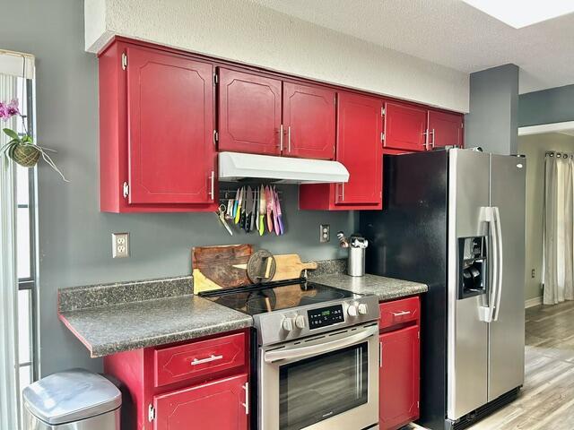 kitchen with red cabinets, under cabinet range hood, appliances with stainless steel finishes, dark countertops, and light wood-type flooring