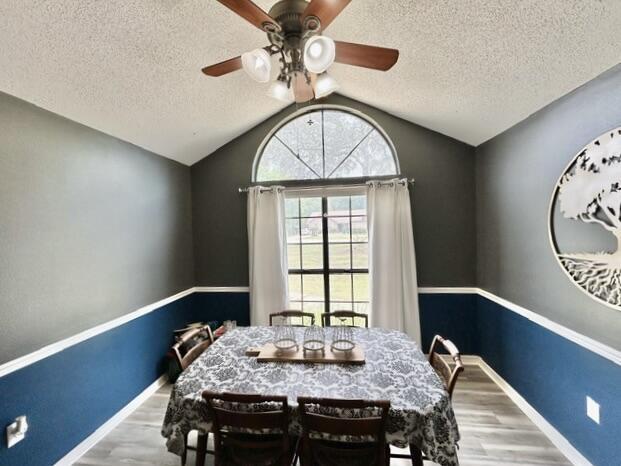 dining space featuring wood finished floors, a ceiling fan, a textured ceiling, and vaulted ceiling