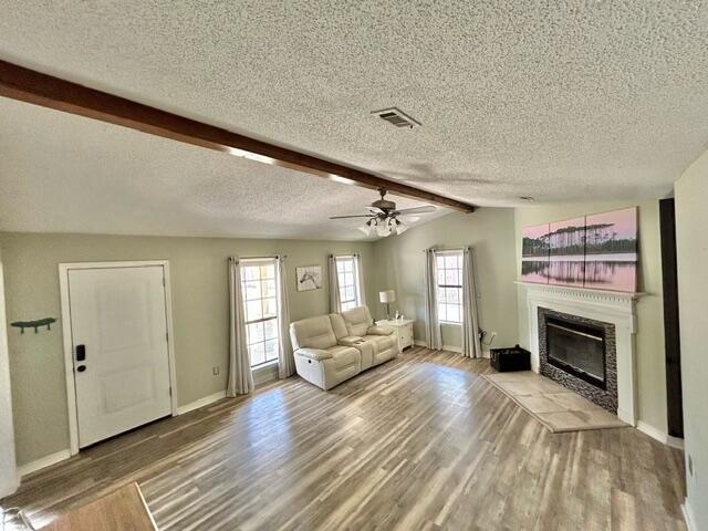 living area with wood finished floors, a glass covered fireplace, baseboards, visible vents, and a textured ceiling