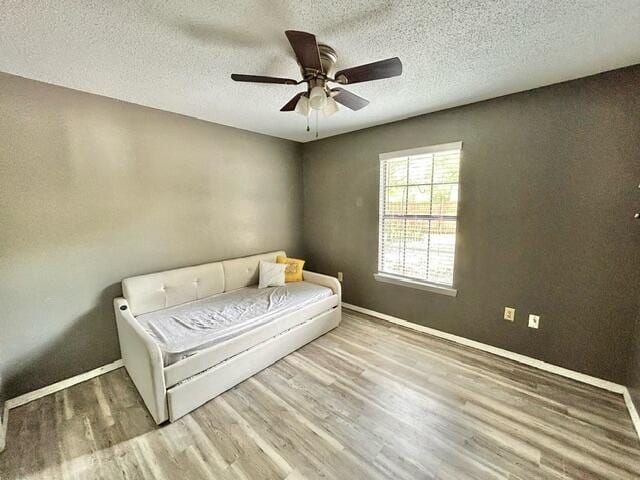 living area featuring a textured ceiling, wood finished floors, a ceiling fan, and baseboards
