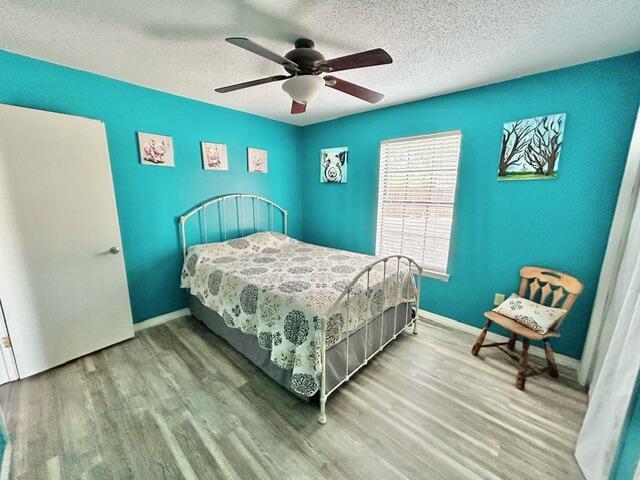 bedroom with baseboards, wood finished floors, ceiling fan, and a textured ceiling