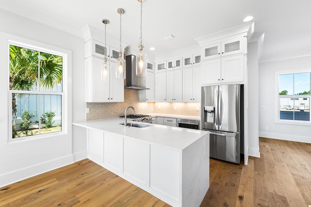 kitchen featuring wall chimney range hood, light countertops, a sink, stainless steel appliances, and decorative backsplash
