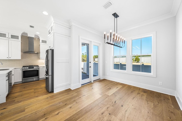 kitchen with crown molding, wall chimney range hood, visible vents, and stainless steel appliances