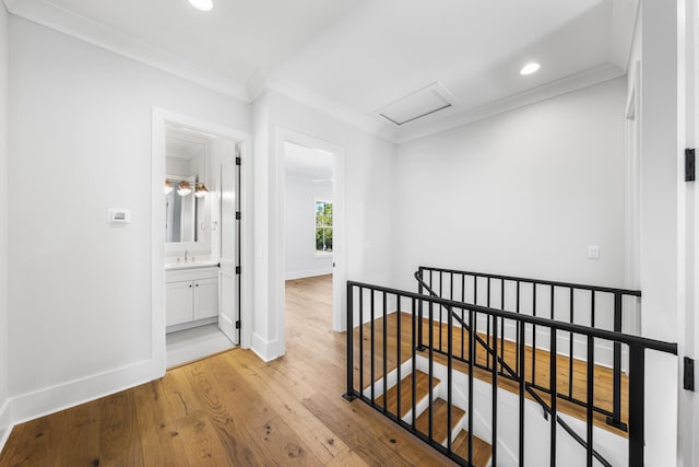 corridor featuring baseboards, ornamental molding, an upstairs landing, attic access, and light wood-style floors