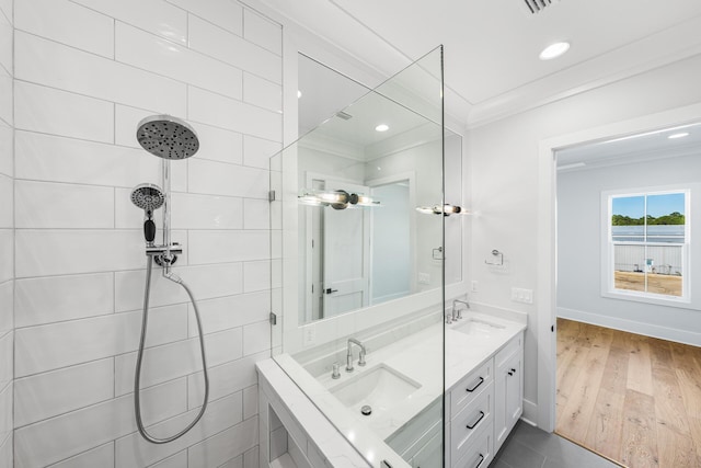 bathroom with crown molding, double vanity, tiled shower, and a sink