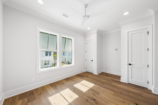 empty room featuring ceiling fan, ornamental molding, visible vents, hardwood / wood-style floors, and baseboards