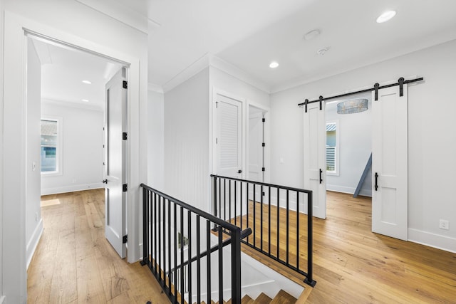 hallway featuring baseboards, ornamental molding, an upstairs landing, a barn door, and light wood-style floors
