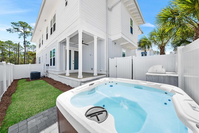 view of property exterior with cooling unit, a ceiling fan, a fenced backyard, a hot tub, and a lawn