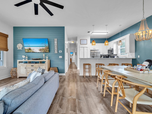 living room with wood finished floors, baseboards, and ceiling fan with notable chandelier