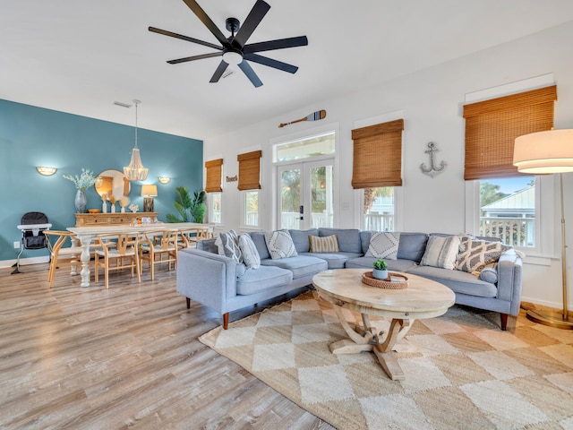 living area with ceiling fan with notable chandelier, baseboards, and light wood finished floors