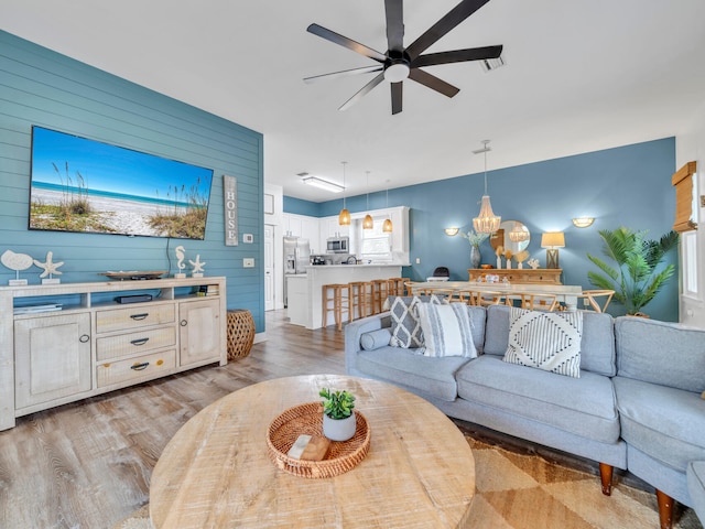 living area with light wood-type flooring, visible vents, wood walls, and ceiling fan