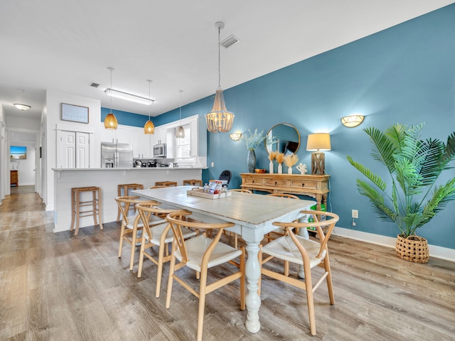 dining area featuring visible vents, light wood finished floors, baseboards, and a notable chandelier