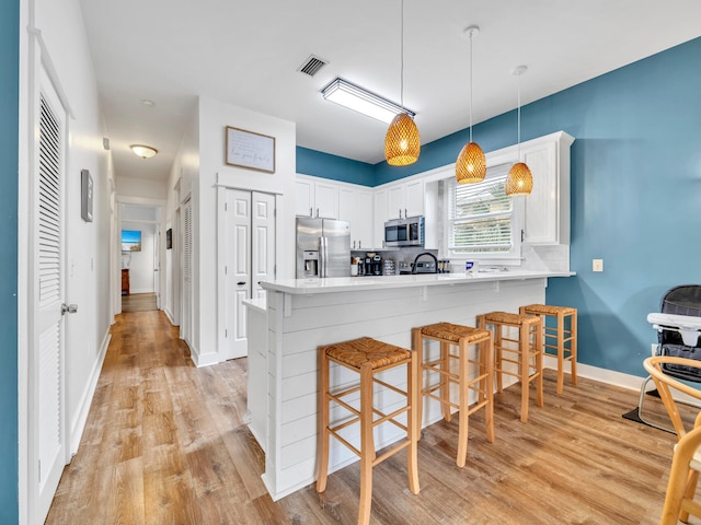 kitchen with white cabinets, a peninsula, light wood-style flooring, a breakfast bar, and appliances with stainless steel finishes