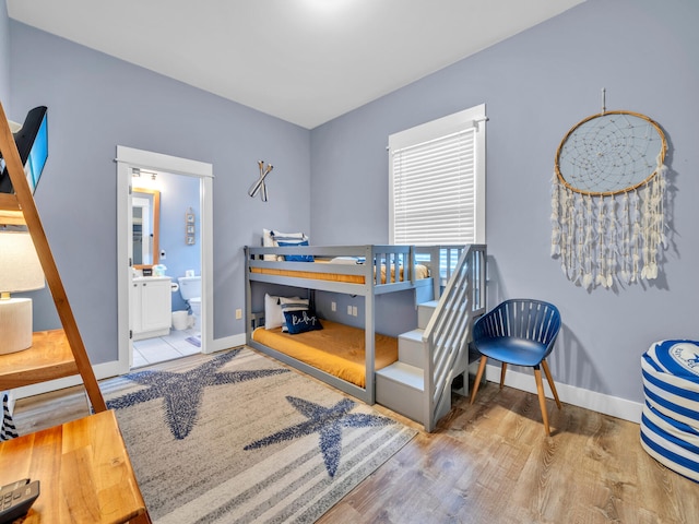 bedroom with wood finished floors, ensuite bath, and baseboards