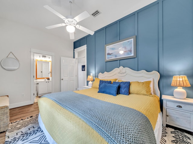 bedroom featuring wood finished floors, ensuite bathroom, ceiling fan, baseboards, and visible vents