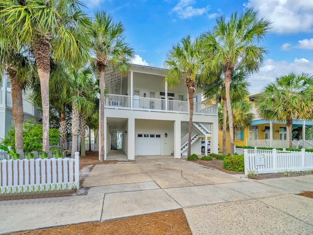 beach home with stairway, driveway, an attached garage, fence, and stucco siding