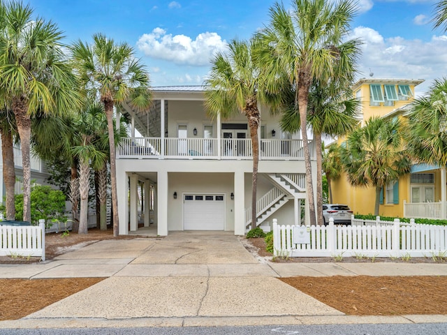 coastal inspired home with stairway, driveway, an attached garage, metal roof, and stucco siding