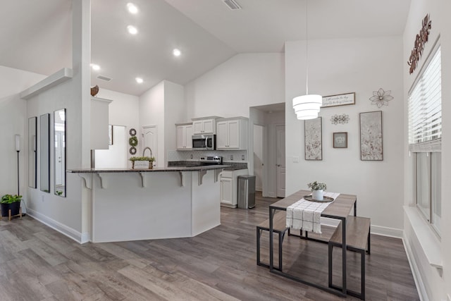 kitchen featuring high vaulted ceiling, a kitchen bar, a peninsula, stainless steel microwave, and dark wood-type flooring