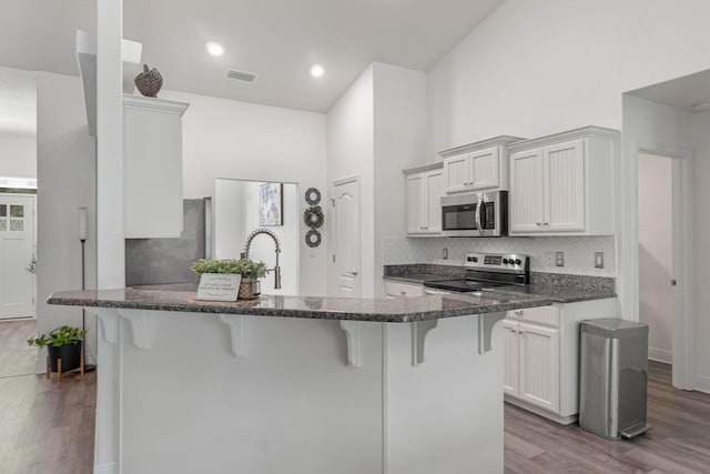 kitchen featuring a kitchen breakfast bar, wood finished floors, stainless steel appliances, and decorative backsplash