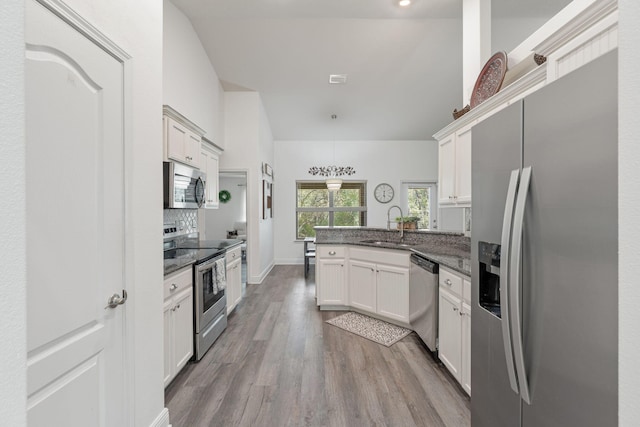 kitchen featuring stainless steel appliances, a sink, white cabinets, a peninsula, and wood finished floors