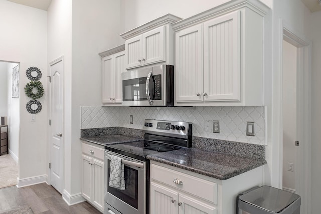 kitchen with decorative backsplash, baseboards, dark stone counters, stainless steel appliances, and dark wood finished floors